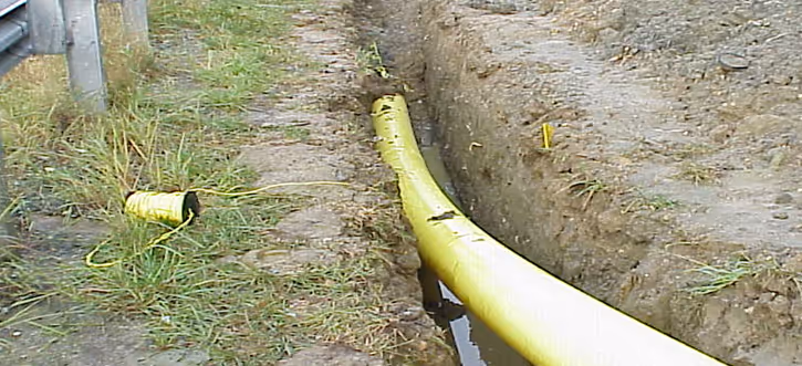 Yellow pipeline laid in a trench alongside a grassy area with a broken pipe piece nearby.