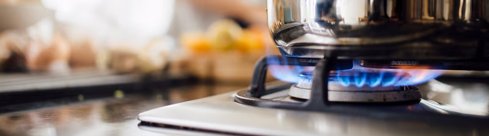 Close-up of a stainless steel pot heating on a gas stove burner with blue flames.