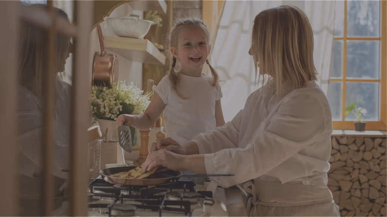 Mother and young daughter smiling while cooking together in a bright kitchen.