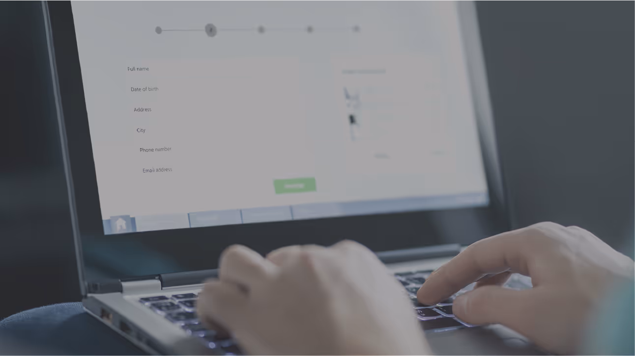 Person typing on a laptop showing a registration form with fields for full name, date of birth, address, city, phone number, and email address.