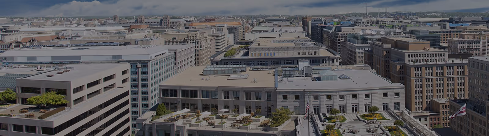 Aerial view of an urban cityscape with multiple office buildings and rooftop terraces under a cloudy sky.