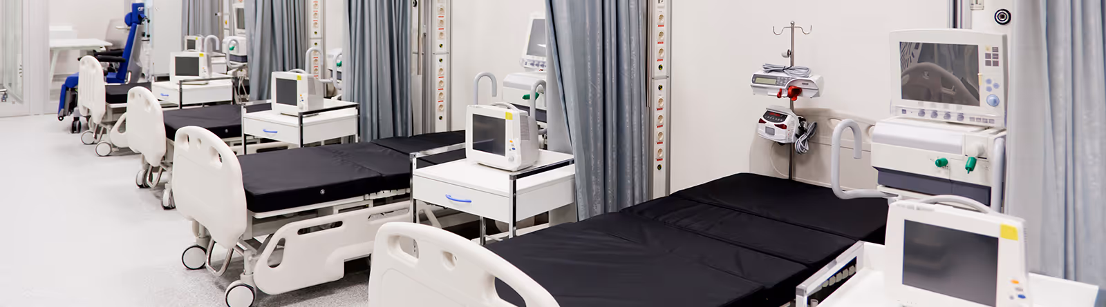 Row of empty hospital beds with black sheets and medical monitors in a clean, modern ward.