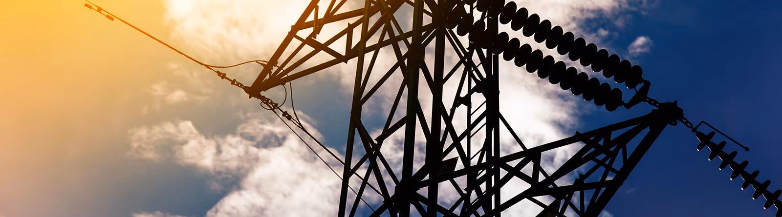 Silhouette of an electricity transmission tower against a partly cloudy sky during sunset.