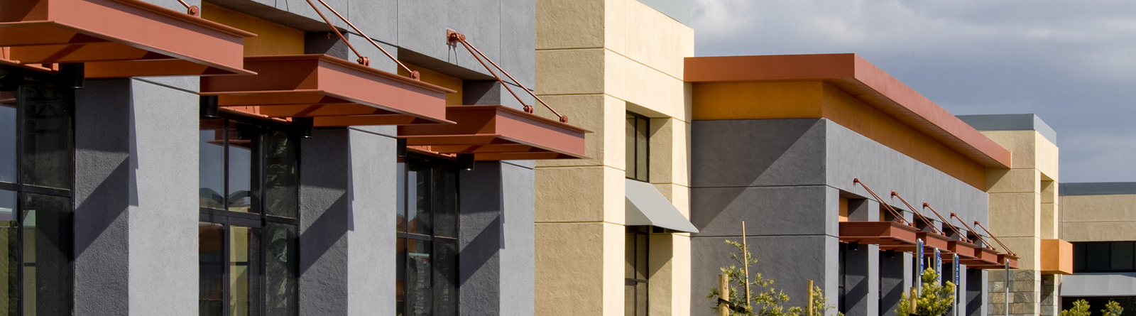 Modern commercial building with gray and beige walls, featuring orange awnings and large glass windows.