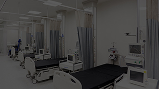 Hospital room with multiple empty beds separated by privacy curtains and medical equipment.