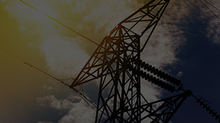 Silhouette of an electricity transmission tower against a partly cloudy sky during sunset.