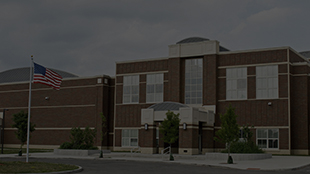 Brick school building with an American flag flying on a pole outside under cloudy sky.