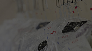 Clothes covered in plastic hanging on hangers with numbered tags at a dry cleaners.