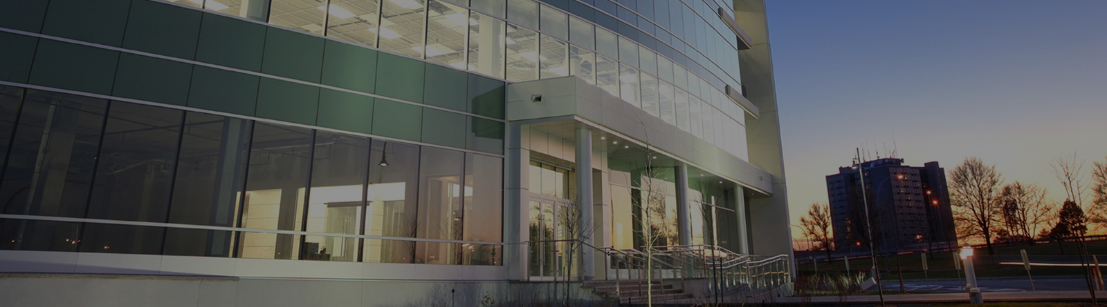 Modern office building with large glass windows and entrance at dusk.
