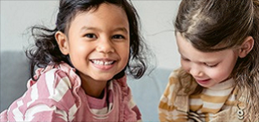Two young girls sitting together, one smiling at the camera and the other looking down.