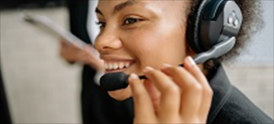 Smiling woman wearing a headset with a microphone, holding the microphone close to her mouth.