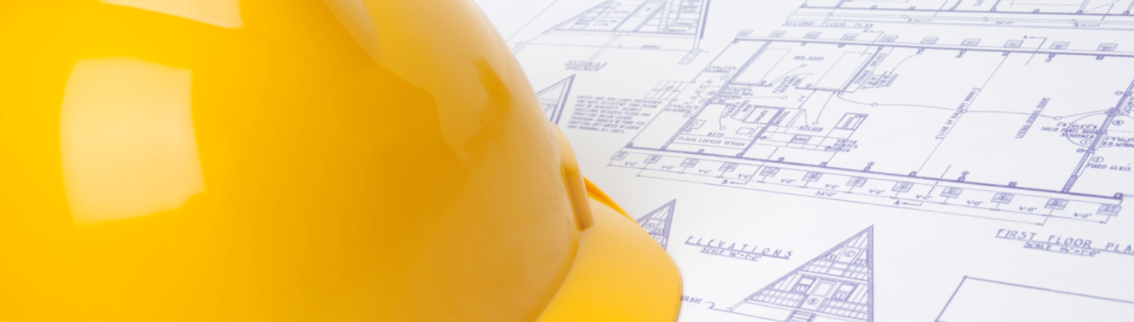 Yellow construction hard hat resting on architectural blueprint drawings.