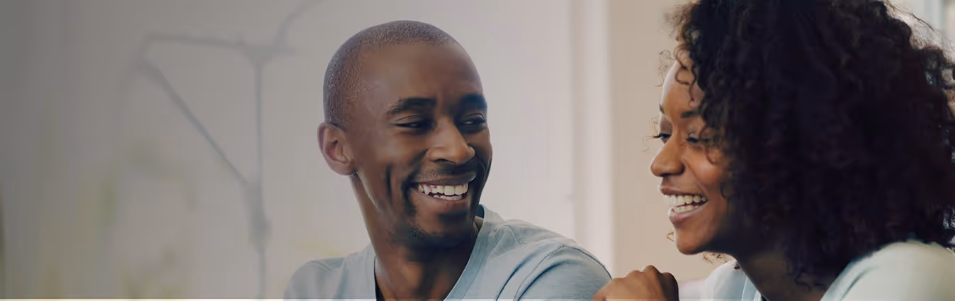 Smiling man and woman facing each other and laughing indoors.