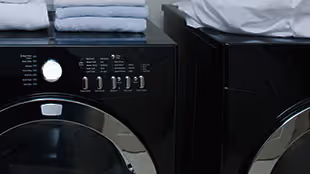 Close-up of the control panel and door of a black front-loading washing machine next to a matching dryer.