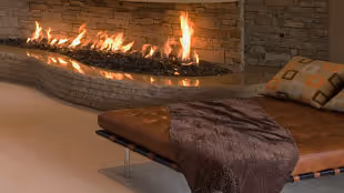 Modern living room with a stone fireplace lit with flames, a brown leather bench topped with a dark throw blanket and a patterned pillow.