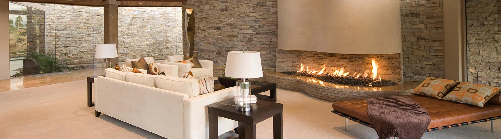 Modern living room with beige couches, a long fireplace with stone wall, and a leather daybed with pillows and a throw.