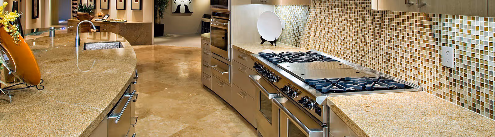 Modern kitchen with beige granite countertops, stainless steel gas stove, built-in oven, mosaic tile backsplash, and curved sink area.