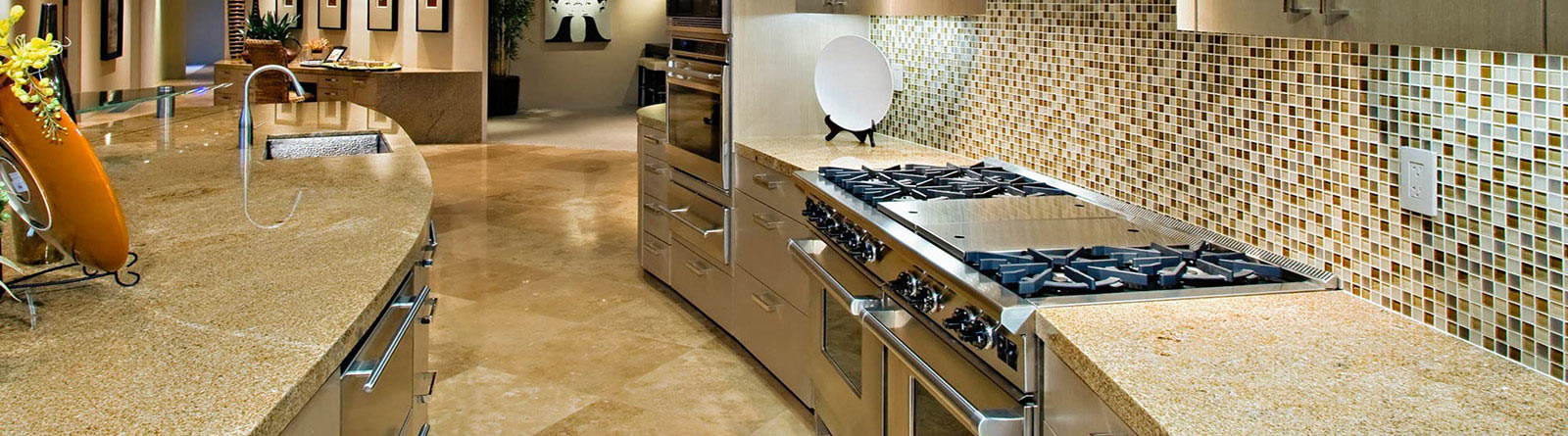 Modern kitchen with beige granite countertops, stainless steel gas stove, built-in oven, mosaic tile backsplash, and curved sink area.
