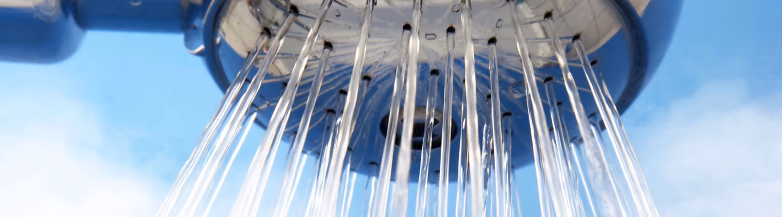Close-up view of water streams flowing downward from a round metal showerhead against a blue sky background.
