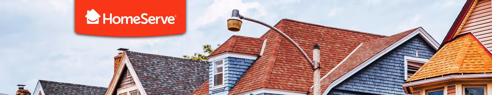 Variety of residential rooftops in different colors and styles under a cloudy sky with the HomeServe logo in red on the top left corner.