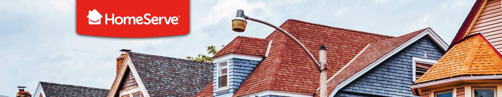 Variety of residential rooftops in different colors and styles under a cloudy sky with the HomeServe logo in red on the top left corner.