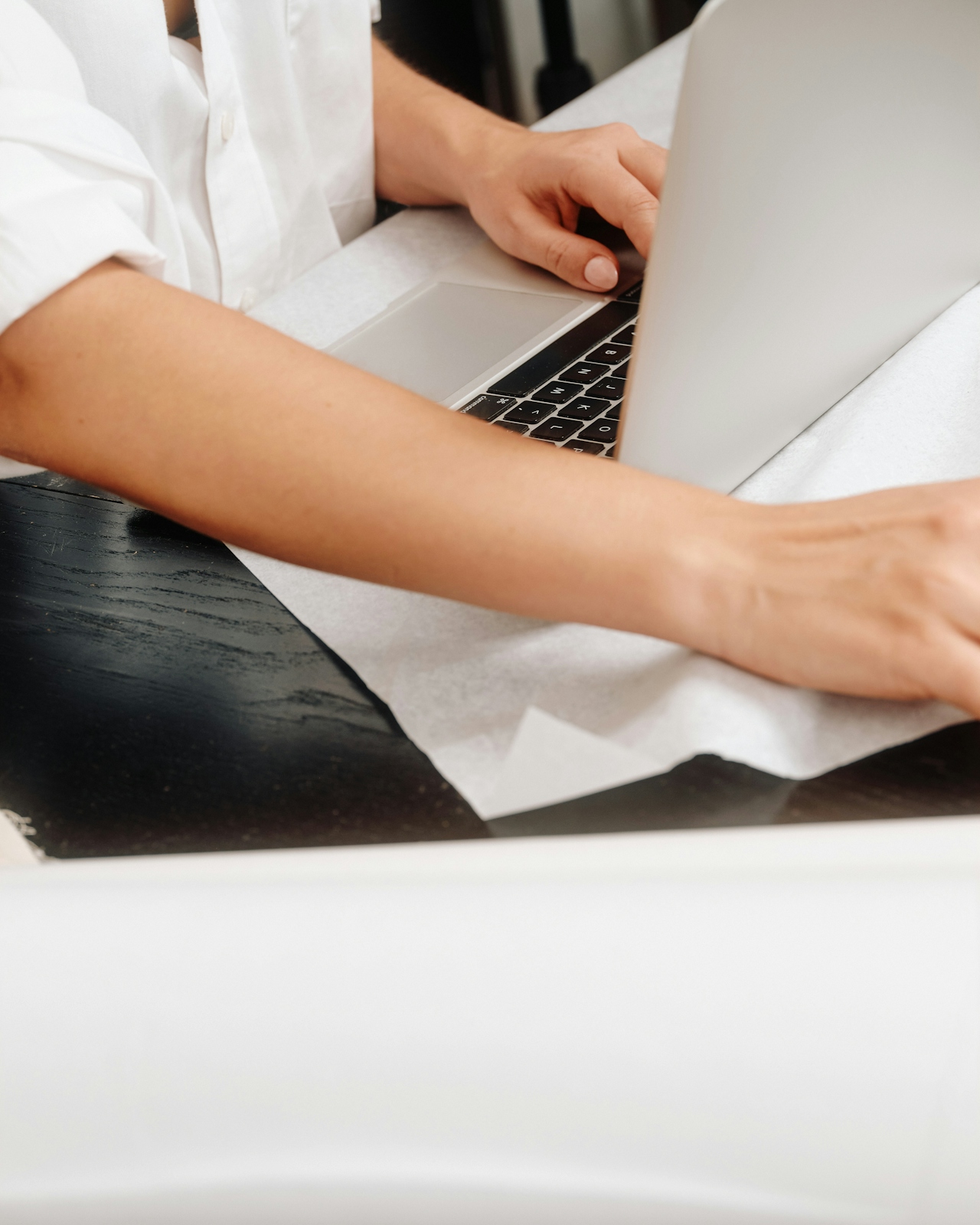 Person tippt auf einem Laptop mit halb geöffnetem Bildschirm auf einem Tisch mit weiße Papierschicht.