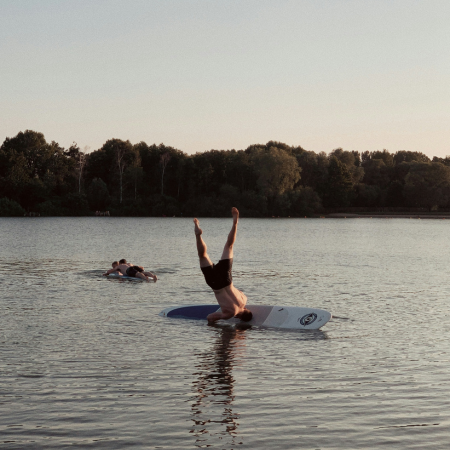 A man falling from a headstand position on a Stand-Up Paddleboard in lake.