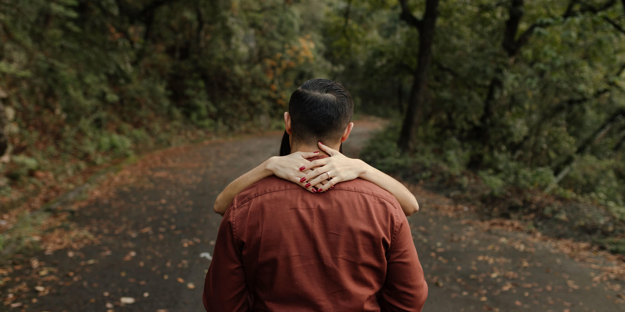 Pareja abrazándose en un camino de bosque con hojas de otoño. Inspiración perfecta para invitaciones de boda de otoño e invierno.