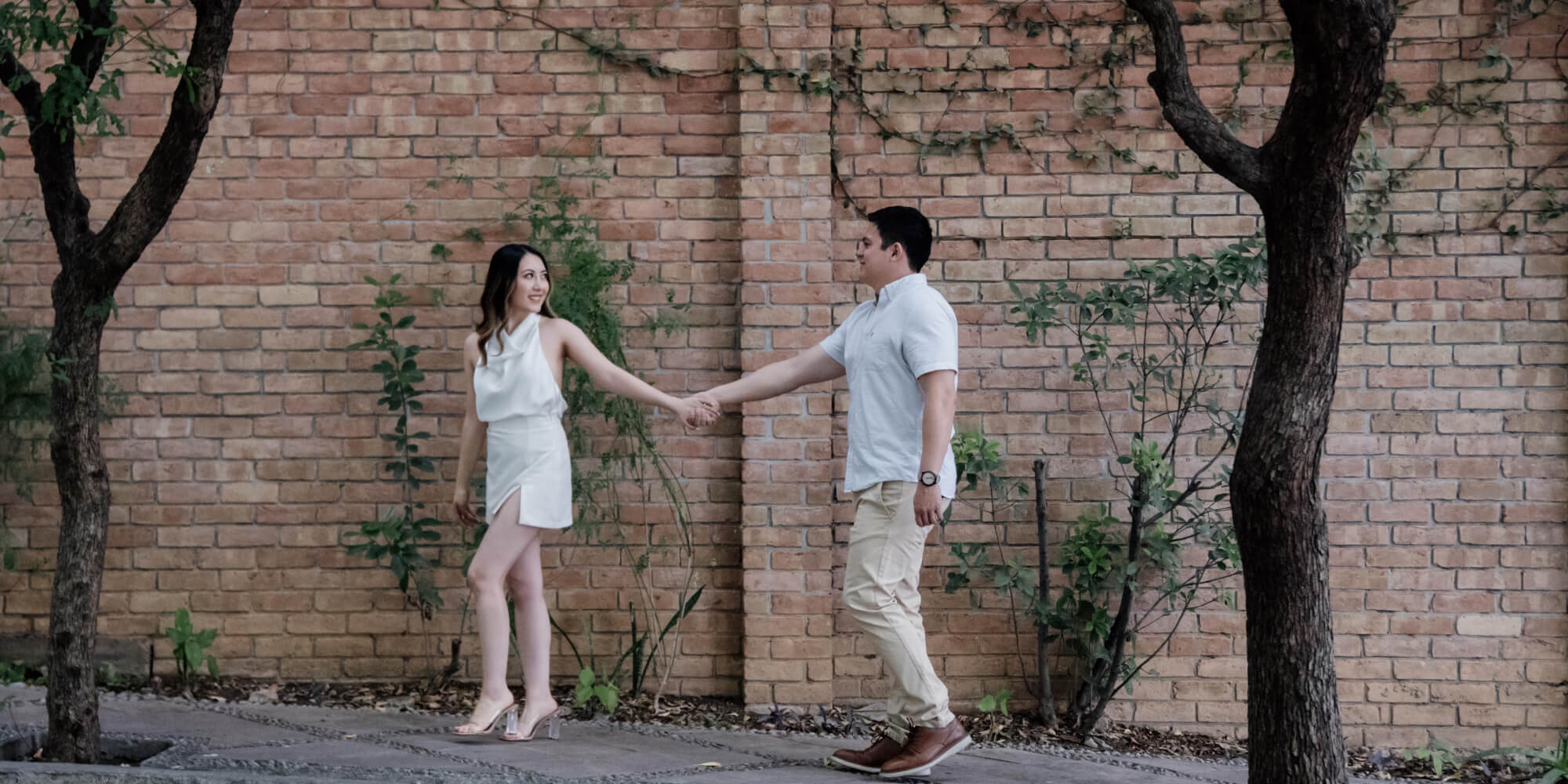 Pareja caminando y tomándose de la mano en una calle de ladrillos. Una foto natural para tu invitación de boda digital.
