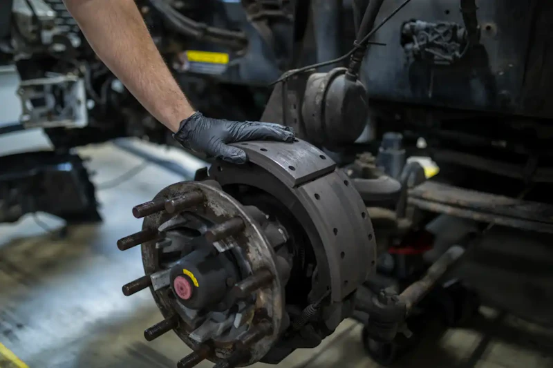 Brake repair on a heavy-duty truck with technician installing brake shoes on an exposed wheel hub.