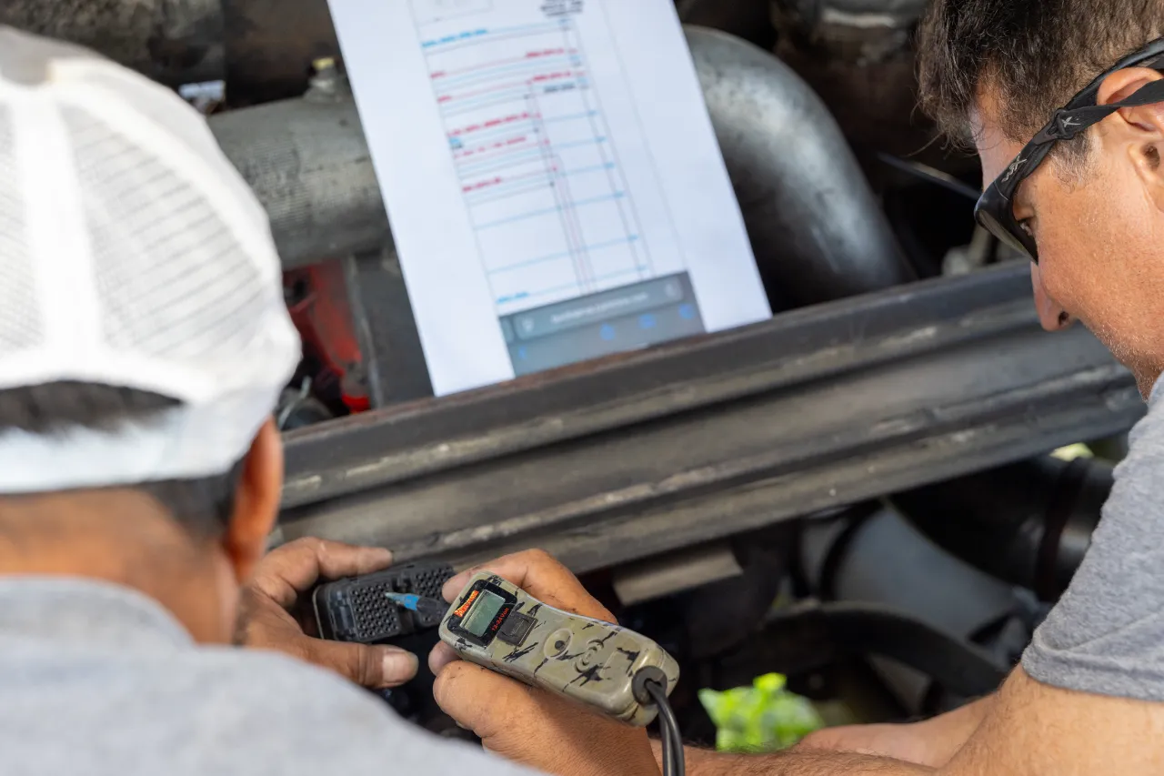 Diagnostics check on a heavy-duty engine with scan tool and tablet; no readable text visible.