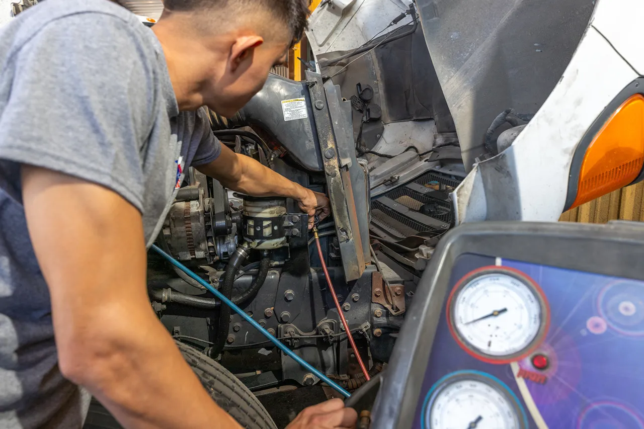 Technician performs preventive maintenance on a heavy-duty truck engine using diagnostic gauges to inspect system performance.