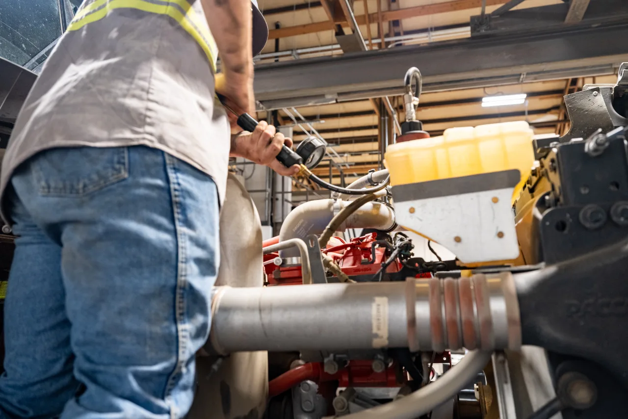 Technician inspects a heavy-duty truck engine for recurring coolant loss in Austin, TX, using a pressure testing tool.