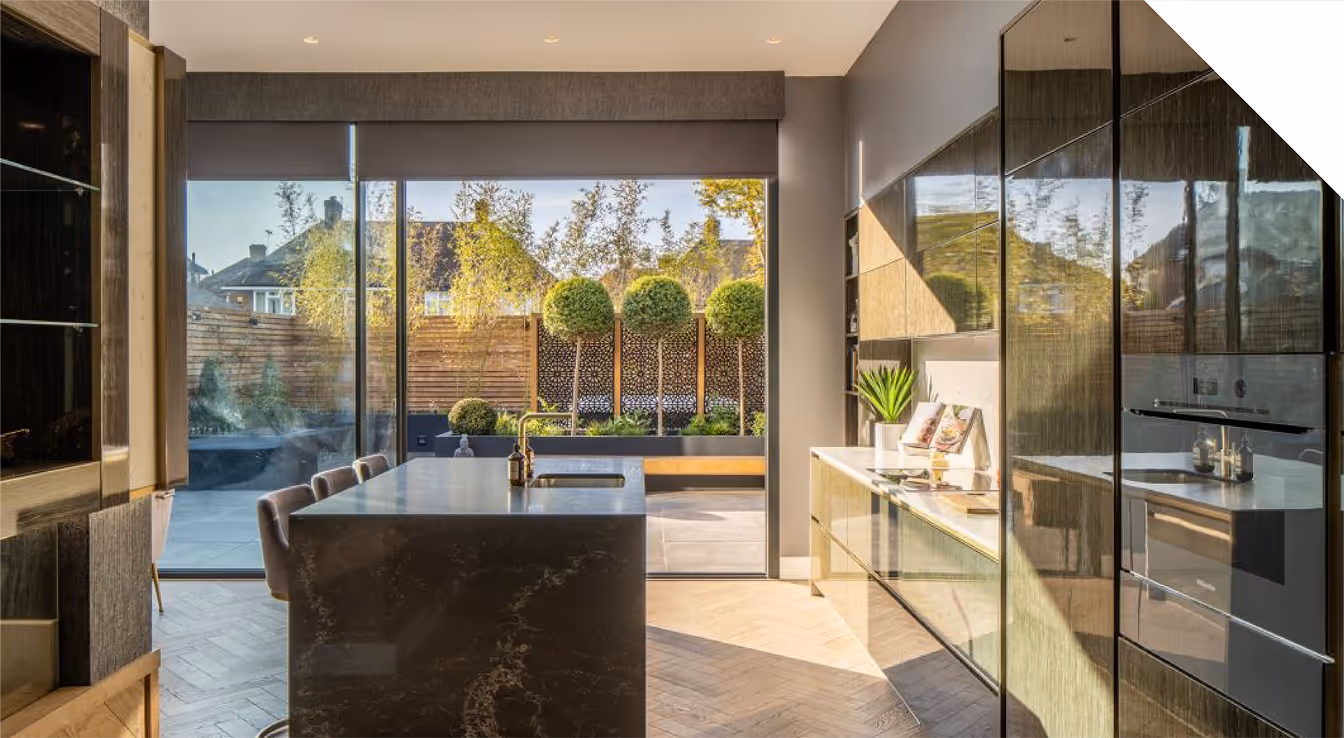 Modern kitchen with a large dark marble island, bar stools, and glass doors opening to a patio with trimmed trees.