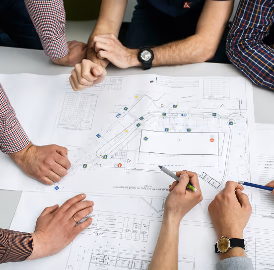 Several people gathered around a table reviewing a large architectural blueprint.