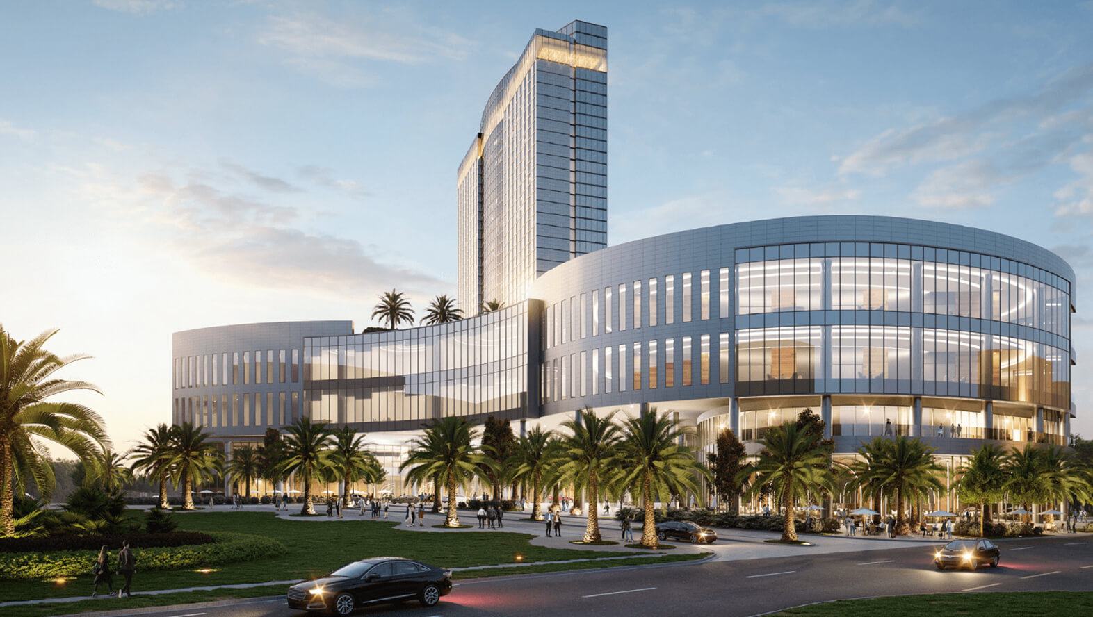 Modern curved glass building with palm trees and pedestrians at sunset near a road with cars.
