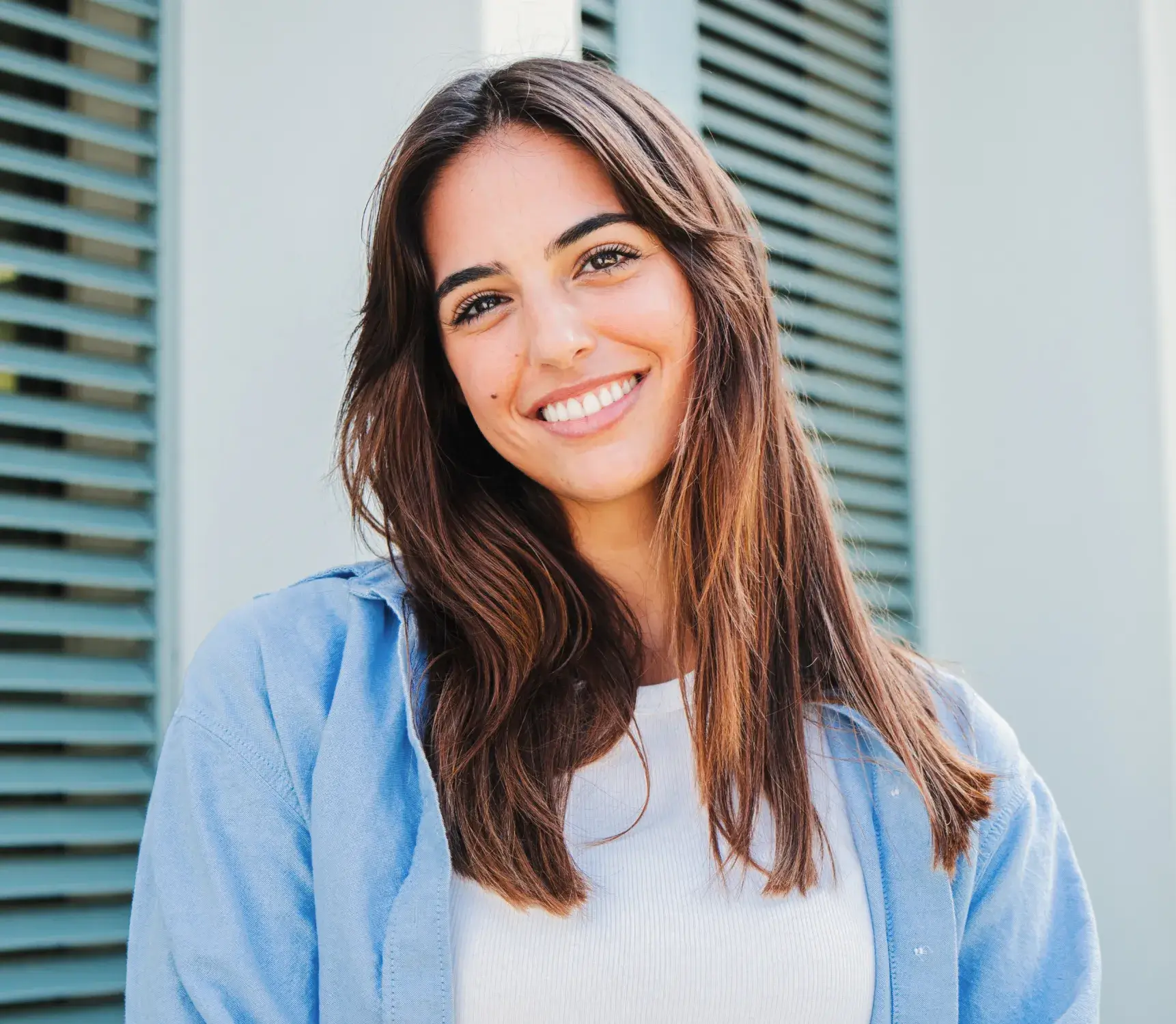 a smiling woman in a blue jacket standing in front of shutters