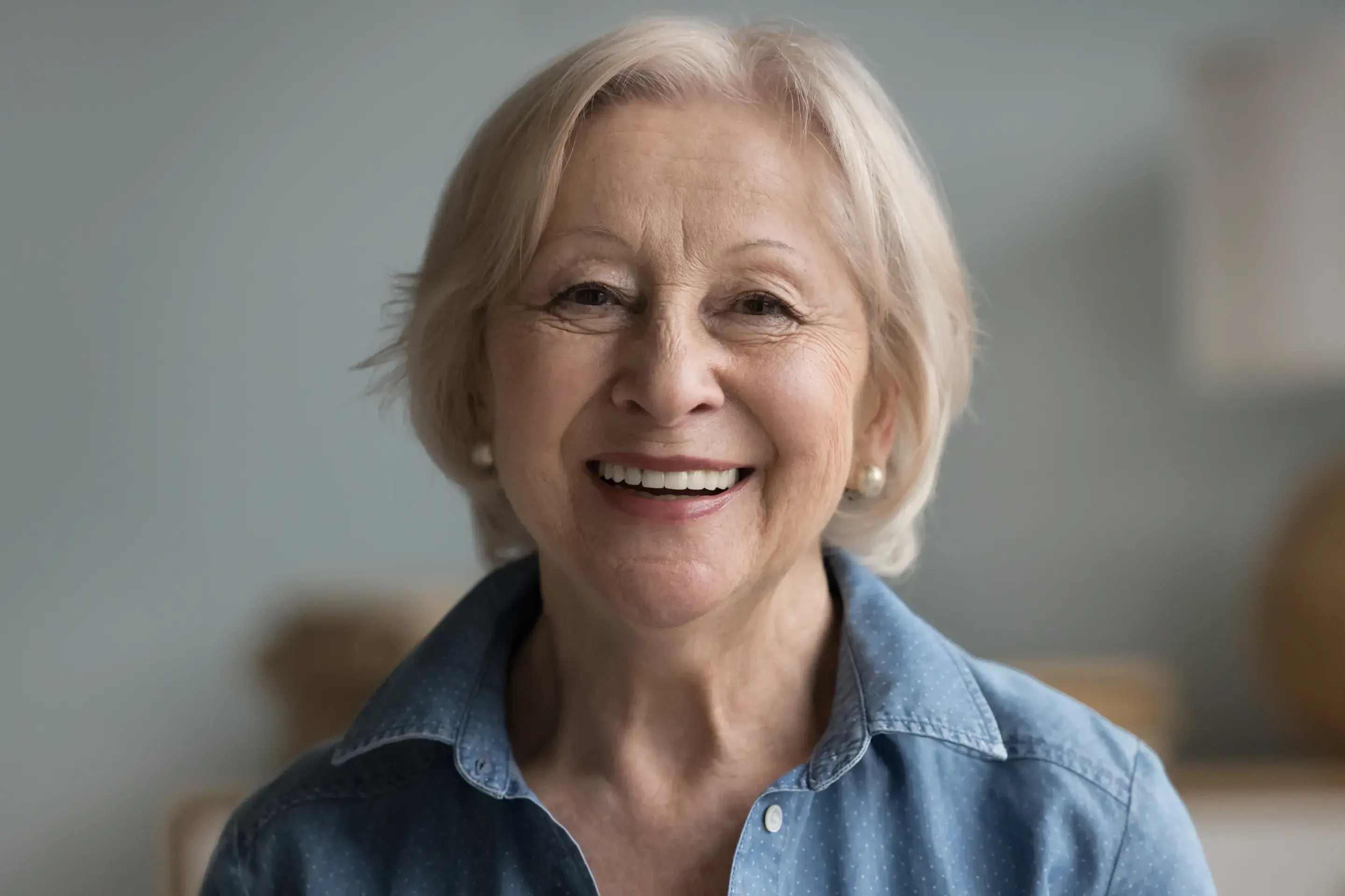 an older woman smiling and wearing a denim shirt