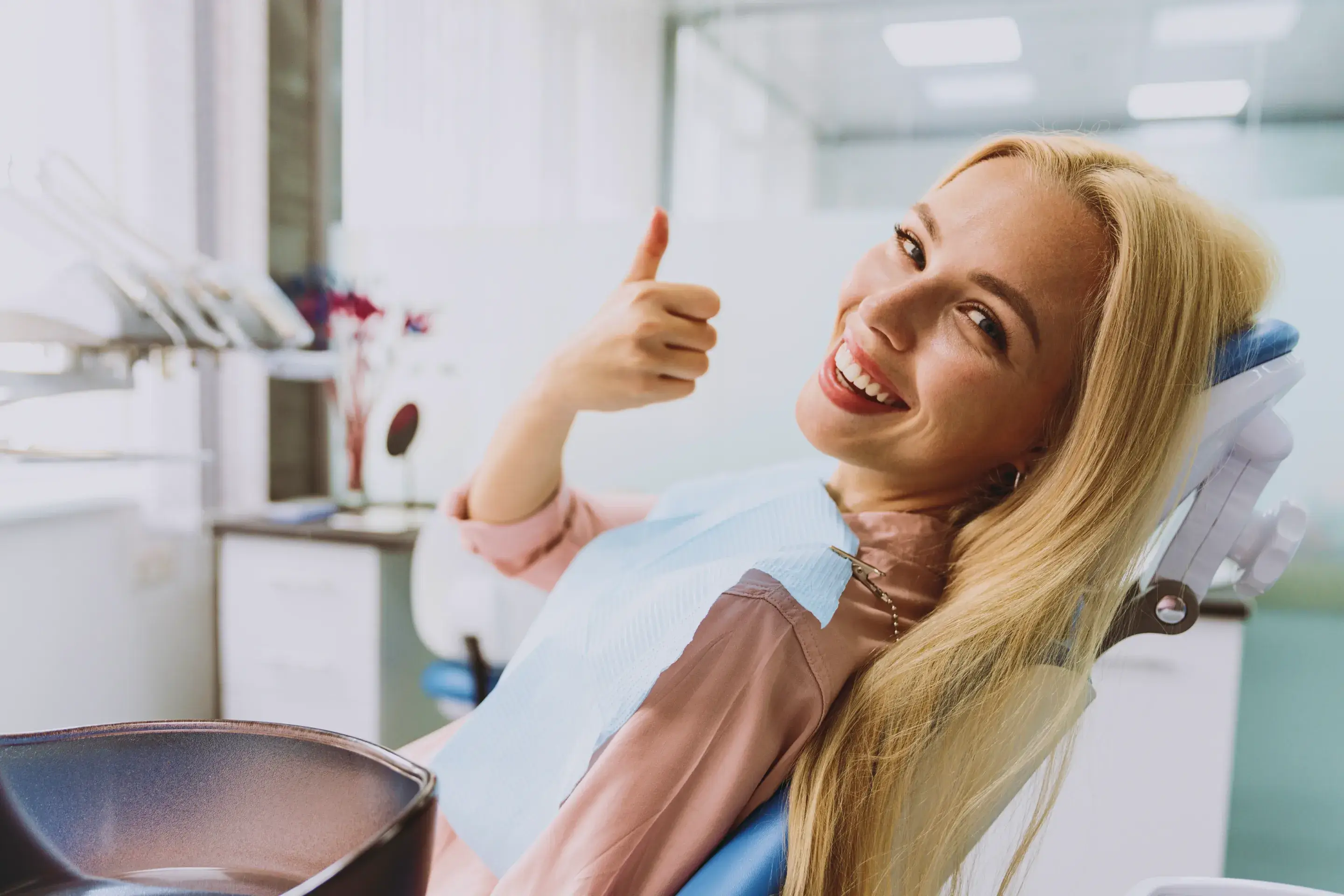 a woman sitting in a dentist chair giving a thumbs up