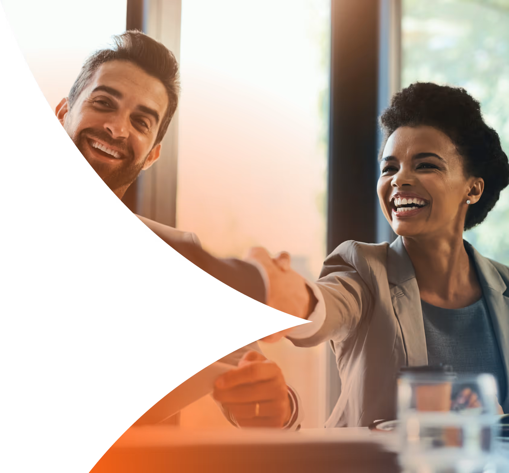 Smiling man and woman shaking hands in a bright office setting.