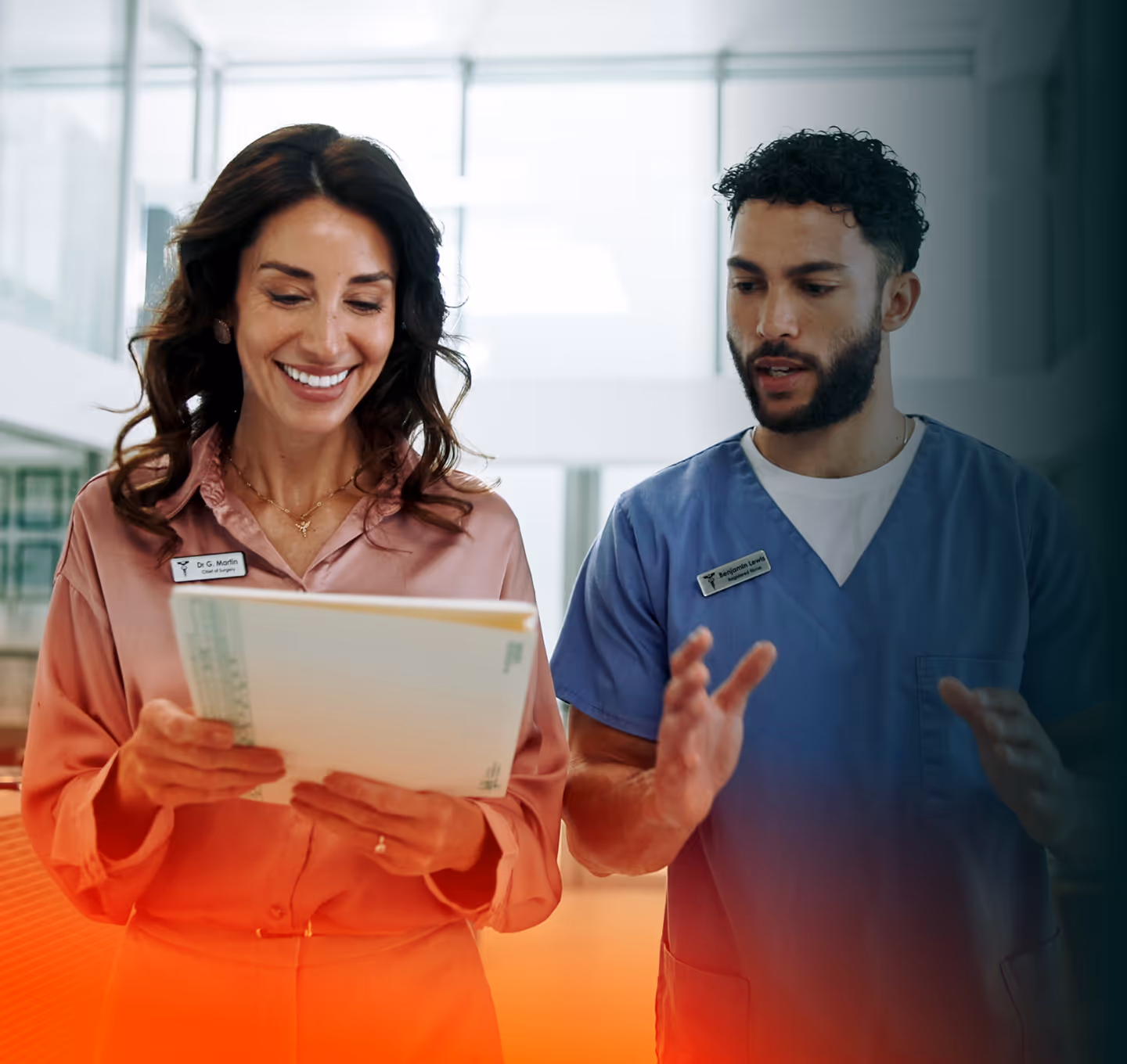 Two healthcare professionals discussing documents in a bright office, a woman in pink blouse smiling and a man in blue scrubs explaining.