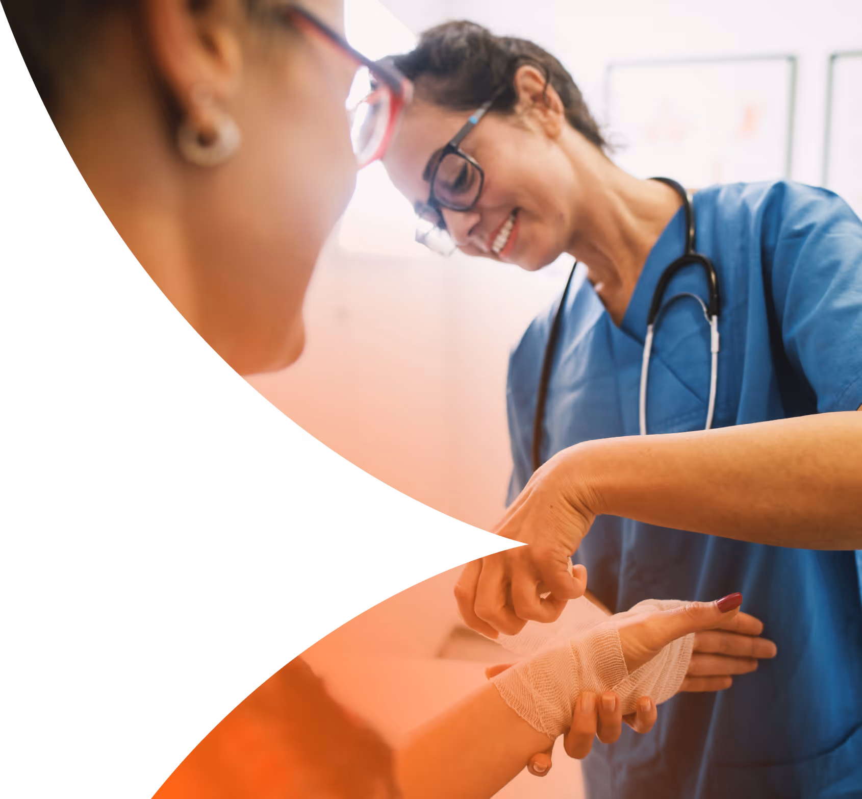 Healthcare professional in blue scrubs smiling while wrapping a bandage around a patient's hand.