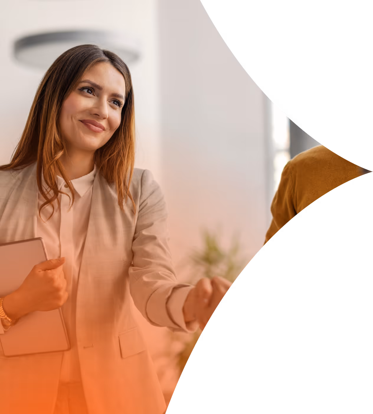 Smiling woman in beige blazer holding a tablet, extending her hand to greet someone.