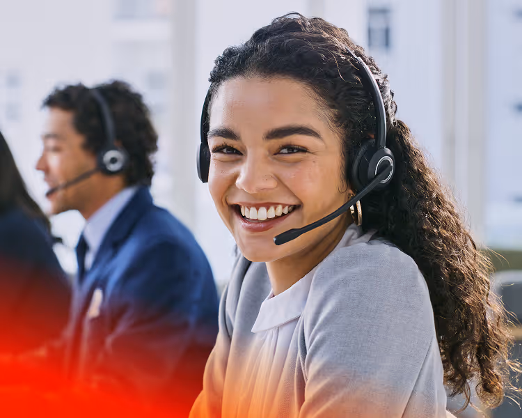 Smiling woman with curly hair wearing a headset in a customer service office.
