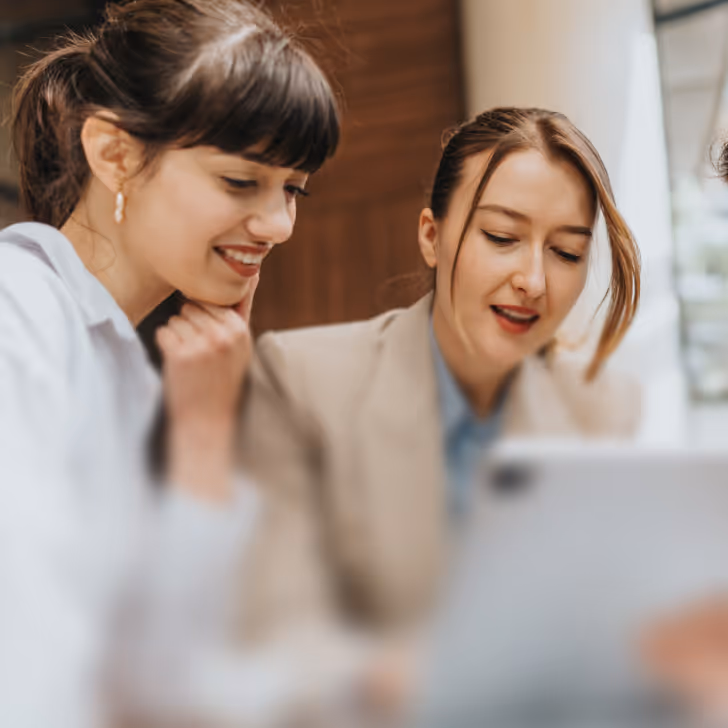 Two women closely looking at a tablet screen, engaged in discussion.