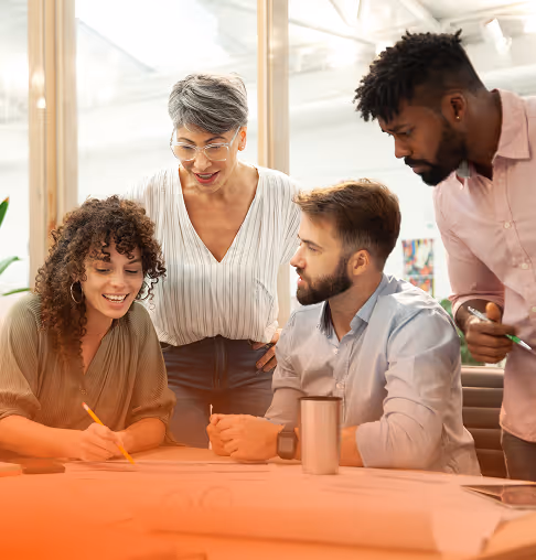 Four diverse coworkers discussing documents at a desk in a bright office space.