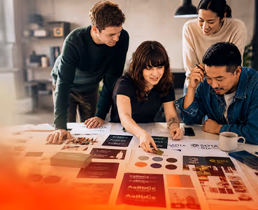 Three people reviewing printed color samples and branding materials around a table.