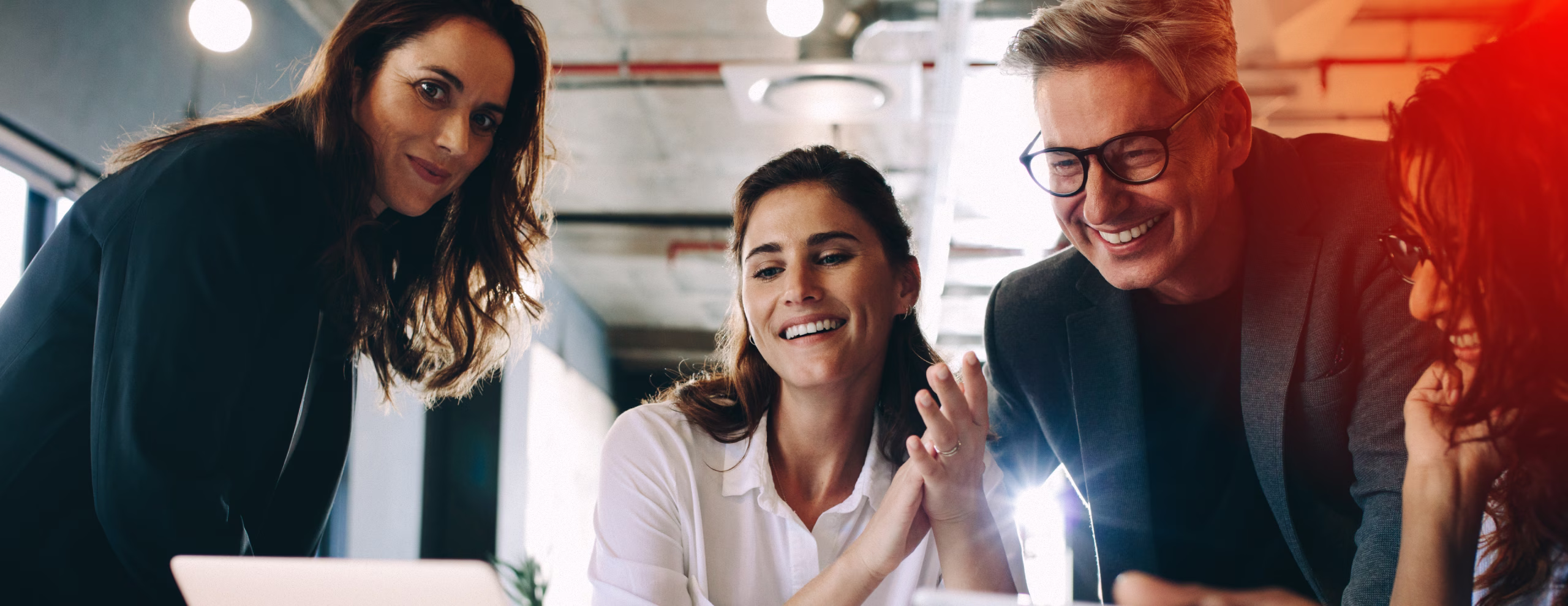 Four diverse colleagues smiling and discussing together around a laptop in a modern office.
