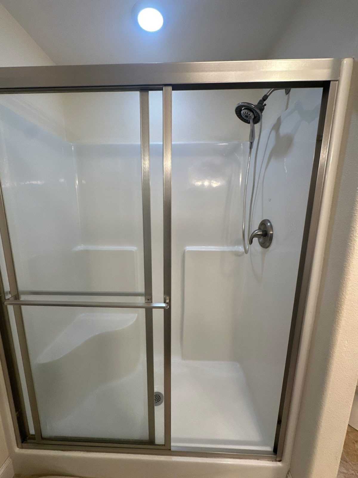 Fiberglass shower with a molded seat and framed sliding glass doors before replacement in Monterey, TN