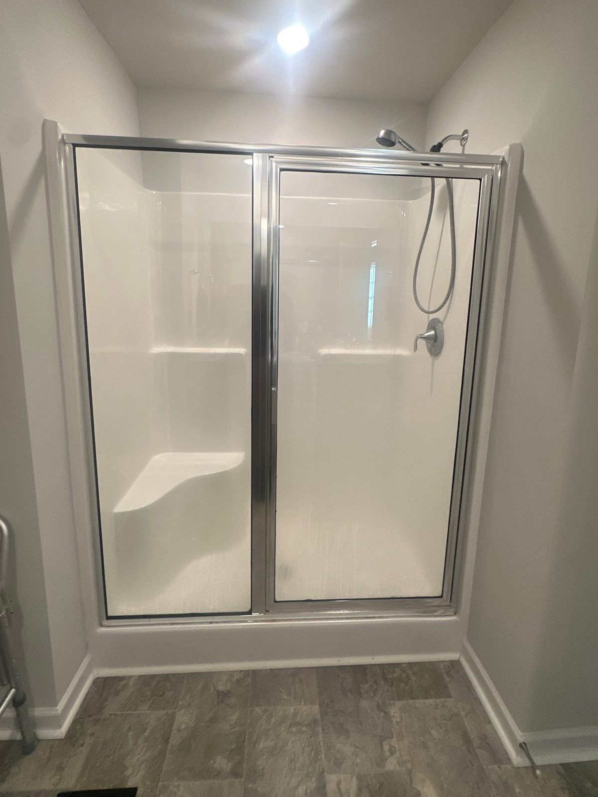 Old fiberglass shower stall with a molded seat and framed sliding glass doors before replacement in Baxter, TN